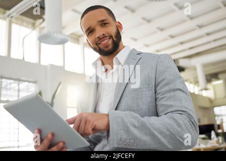 Porträt eines jungen, glücklichen Geschäftsmannes aus gemischtem Rennen, der in einem Büro an einem digitalen Tablet arbeitet. Ein hispanischer männlicher Chef lächelt und hält ein digitales Tablet Stockfoto