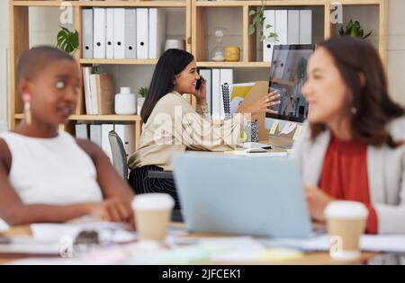 Serious ehrgeizige indische Geschäftsfrau mit Mobiltelefon, um mit Kunden zu sprechen, während sie Bürocomputer verwendet. Selbstbewusster ethnischer Profi sitzt dahinter Stockfoto