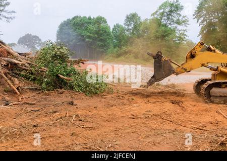 Während der Entwurzelung von Bäumen und der Entwaldung arbeitet ein Traktor an dem Prozess, um das Land für den Neubau eines Hauses vorzubereiten. Stockfoto