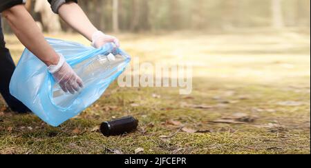 Der junge Mann sammelt Plastikmüll, Glas vom Boden. Ein Freiwilliger reinigt den Park an einem sonnigen, hellen Tag. Clearing, Umweltverschmutzung, Ökologie und Plasti Stockfoto
