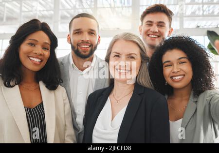 Porträt einer Gruppe von fünf fröhlichen, vielfältigen und positiven Geschäftsleuten, die zusammen ein Selfie bei der Arbeit machen. Junger glücklicher kaukasischer Geschäftsmann nimmt einen Stockfoto