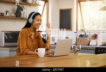 Junge, glückliche Geschäftsfrau mit gemischtem Rennen winkt während eines virtuellen Meetings mit einem Laptop zu Hause. Eine hispanische Geschäftsfrau sprach und grüßte Stockfoto
