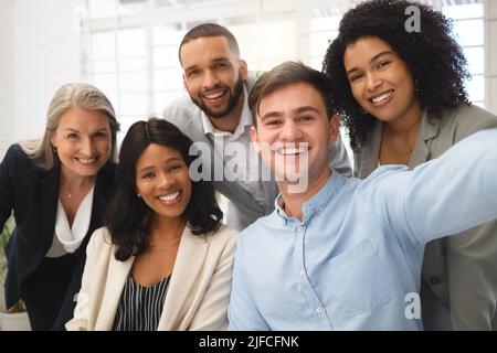 Eine Gruppe von fröhlichen, vielfältigen Geschäftsleuten, die zusammen ein Selfie bei der Arbeit machen. Glücklicher junger kaukasischer Geschäftsmann, der ein Foto mit seinem Inhalt macht Stockfoto