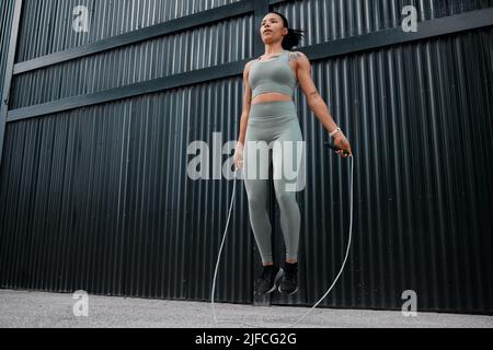 Eine junge afroamerikanische Athletin, die im Freien in der Stadt mit einem Springseil hüpft. Schönes und engagiertes gemischtes Rennen Stockfoto