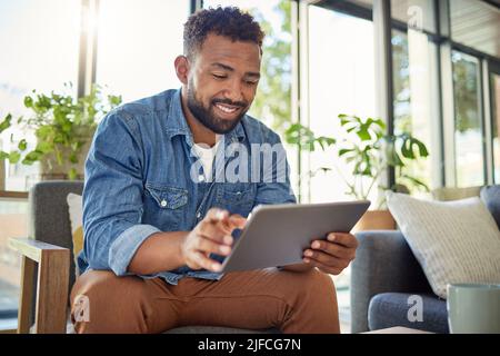 Hispanischer Mann mit seinem digitalen Tablet zu Hause. Der junge Junggeselle verwendet sein drahtloses Gerät in seiner Wohnung. Ein hübscher Mann, der auf seinem Computer im Internet surft Stockfoto