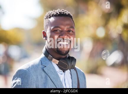Afroamerikanischer Mann, der Kopfhörer trägt, während er in der Stadt unterwegs ist. Porträt eines glücklichen, hübschen schwarzen Mannes, der auf seinem täglichen Weg zur Arbeit Musik genießt Stockfoto