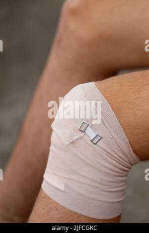 Knie des Jungen nach der Verstauchung mit einem elastischen Band zum Schutz des beschädigten Gelenks Stockfoto