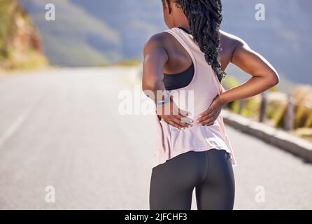Rückansicht einer aktiven, nicht erkennbaren Frau, die ihren Rücken vor Schmerzen beim Training im Freien hält. Nahaufnahme eines Athleten, der mit einem schmerzhaften Unterleidensweg leidet Stockfoto