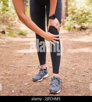 Nahaufnahme einer athletischen jungen Frau, die ihr Knie vor Schmerzen hält, während sie im Freien trainiert. Aktive Frau trägt Laufschuhe und leidet an Stockfoto