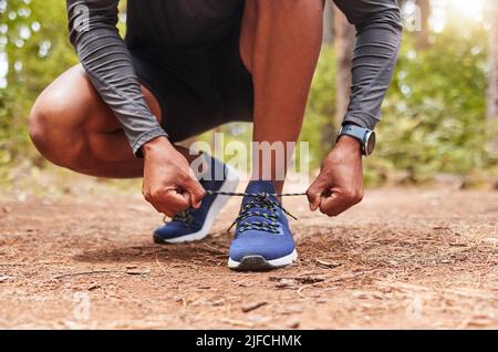 Nahaufnahme eines sportlichen Mannes, der seine Schnürsenkel beim Training im Freien bindet. Aktiver Mann mit Laufschuhen, während er für ein Training in der Natur unterwegs ist Stockfoto