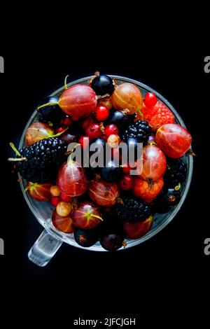 Himbeeren, Maulbeeren, Stachelbeeren und Johannisbeeren in einer Tasse auf schwarzem Hintergrund. Stockfoto