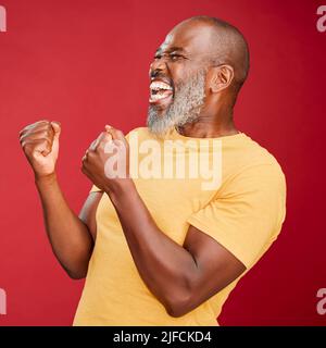 Reifer afroamerikanischer Mann mit einem lächelnden Bart und jubelnden Fäusten, der vor einem roten Studiohintergrund steht. Glücklich, Erfolg Stockfoto