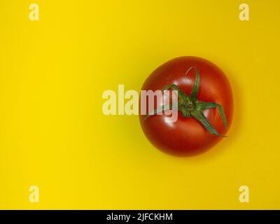 Tomate auf farbigem Papier. Gewächshaus-Tomate auf gelbem Hintergrund. Heller Gemüsehintergrund. Hintergrund von Tomaten. Stockfoto