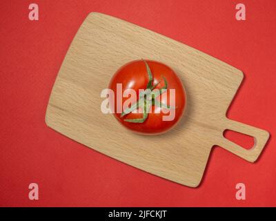 Tomate auf farbigem Papier. Gewächshaus Tomate auf einer Küche kleines Brett. Heller Gemüsehintergrund. Stockfoto