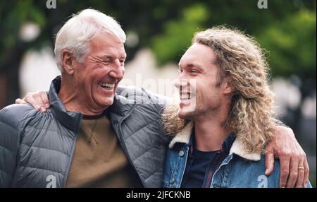 Ein reifer Mann umarmte seinen jungen Sohn während eines Tages im Park. Ein fröhlicher junger Mann, der sich mit seinem Vater im Park entspannt. Ein älterer Mann mit seinem Arm Stockfoto
