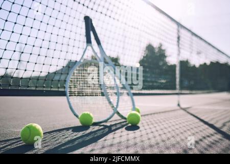 Gruppe von Tennisbällen und Schlägern gegen ein Netz auf einem leeren Platz in einem Sportverein während des Tages. Tennis spielen ist Bewegung, fördert die Gesundheit Stockfoto