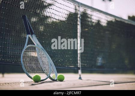 Gruppe von Tennisbällen und Schlägern gegen ein Netz auf einem leeren Platz in einem Sportverein während des Tages. Tennis spielen ist Bewegung, fördert die Gesundheit Stockfoto