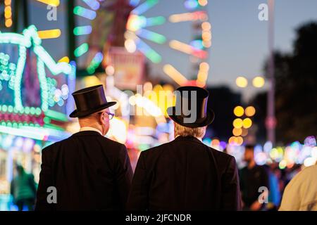 Hannover, Deutschland. 01.. Juli 2022. Zwei Menschen mit Kopfbedeckung laufen über das Schützenfest am Schützenplatz. Nach einer zweijährigen Pause aufgrund der Corona findet vom 01. Bis 10. Juli wieder das Schützenfest Hannover auf dem Schützenplatz statt. Kredit: Michael Matthey/dpa/Alamy Live Nachrichten Stockfoto