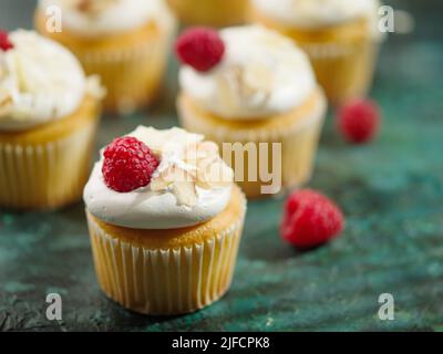 Viele appetitliche Beerenmuffins mit leichter, luftiger Creme, Himbeeren, Mandeln auf dunkelgrünem Hintergrund. Bankett, Picknick, Geburtstag. Werbung, banne Stockfoto