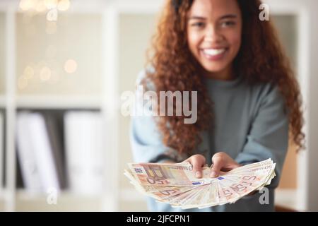 Eine glückliche junge Frau mit gemischter Rasse, die mit zwei Händen Bargeld hält und sich reich fühlt. Aufgeregt hispanische Frau zeigt Geld nach Budgetierung Finanzen und Stockfoto