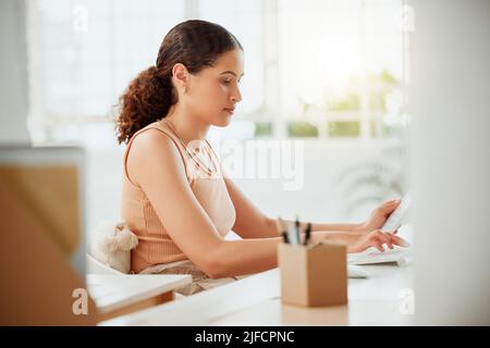 Eine junge hispanische Geschäftsfrau, die während der Arbeit an einem Computer in einem Büro einen Rechner benutzt. Fokussierter Unternehmer, der Finanzen für Steuern berechnet Stockfoto