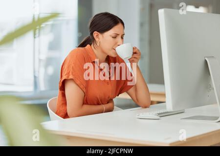 Eine hispanische Geschäftsfrau, die warmen Tee als Heilmittel gegen Magenschmerzen trinkt, während sie sich in einem Büro an menstruellen Magenkrämpfen erkrankt fühlt. Kranker Mitarbeiter Stockfoto
