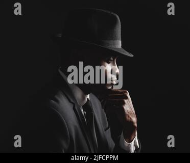 afroamerikanischer Mann posiert vor einem schwarzen Hintergrund und trägt einen Anzug und Hut, der achtsam und traurig aussieht.trauernde Person, die an Depressionen und Angstzuständen leidet Stockfoto