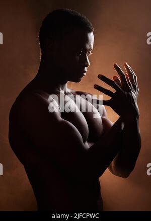 Ein hübscher, muskulöser junger afroamerikanischer Mann im Studio vor dunklem Hintergrund. Ein Macho-Athlet, der nachdenklich und isoliert auf Schwarz aussieht Stockfoto