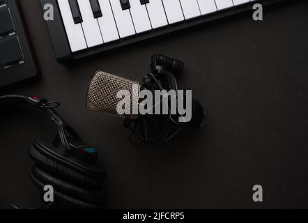 Nahaufnahme. Midi-Keyboard, Studiomikrofon und Kopfhörer auf grauem Hintergrund. Low-Angle-Ansicht. Monochromes Bild. Musik, Gesang, Arbeit mit Sound, Voic Stockfoto