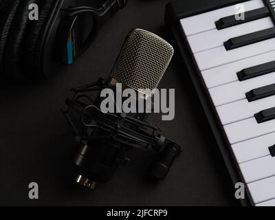 Auf dunkelgrauem Hintergrund ein Midi Keyboard, Synthesizer, Studiomikrofon und Studiokopfhörer. Musik, Gesang, Radio, Fernsehen, Tonstudio. Stockfoto