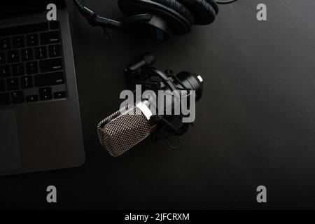 Laptop, Studiomikrofon und Studiokopfhörer auf dunkelgrauem Hintergrund. Low-Angle-Ansicht. Arbeitsplatz eines Musikers, Komponisten, Toningenieurs. Sound wo Stockfoto