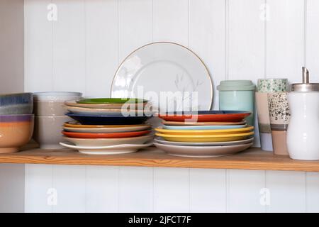 Holzregal mit Küchenutensilien, rustikaler Stil. Geschirr, Teller und Schüsseln stehen auf einem Regal in der Küche. Schrank mit bunten Geschirr, Stockfoto