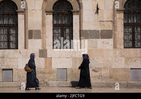 Zwei muslimische Frauen, die auf dem Bürgersteig vor der Alaeddin-Moschee in Konya, Türkei, spazieren. Stockfoto