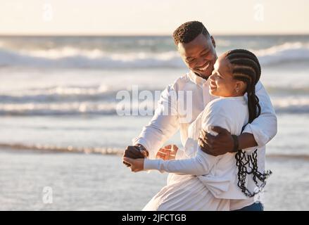 Liebevolles junges Paar, das einen romantischen Moment hat, während es einen Tanz teilt und zusammen am Strand verbringt. Glückliche afroamerikanische Liebhaber, die verspielt sind und Stockfoto