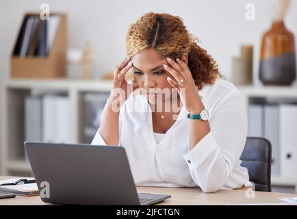 Junge Geschäftsfrau mit gemischter Rasse, die bei der Arbeit an einem Laptop in einem Büro Kopfschmerzen hat. Einer betonte hispanische Geschäftsleute Stockfoto