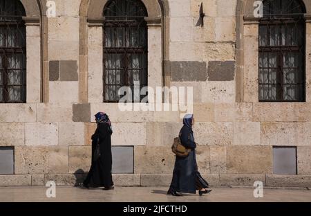 Zwei muslimische Frauen, die auf dem Bürgersteig vor der Alaeddin-Moschee in Konya, Türkei, spazieren. Stockfoto