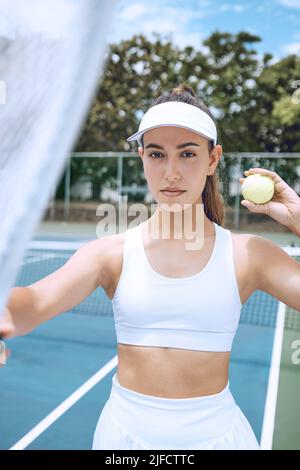 Selbstbewusste junge Tennisspielerin mit Tennisschläger und Ball. Hispanische Frau bereit für ihr Tennisspiel im Club. Sportlerin bereit für Stockfoto
