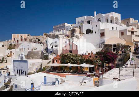 Häuser, Restaurants und Bougainville Blumen in Oia Dorf, Santorini, Griechenland. Stockfoto