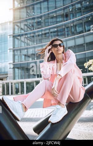 Eine junge trendige und selbstbewusste Mixed-Race-Frau, die stylisch aussieht, während sie posiert und Zeit in der Stadt verbringt. Modische hispanische Frau trägt rosa Stockfoto