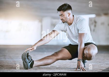 Fit jungen Mann streckt seine Beine beim Training im Freien. Hübscher indischer Mann, der seine Zehen berührt, um sich für einen Lauf aufzuwärmen Stockfoto