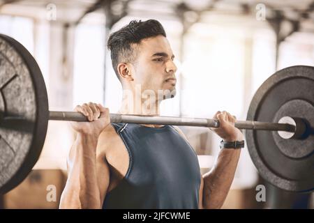 Konzentrierter Bodybuilder, der schwere Gewichte hebt. Aktiver Athlet, der mit einer schweren Langhantel Armmuskulatur baut. Starker Trainer, der sein Workout-Programm im macht Stockfoto