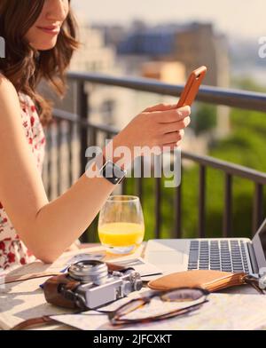 Um darüber zu bloggen, erlebnisses. Aufnahme einer jungen Frau mit einem Smartphone beim Frühstück auf dem Balkon einer Wohnung mit Blick auf Stockfoto