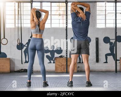 Zwei aktive kaukasische Athleten von hinten strecken ihre Arme und Trizeps, indem sie den Ellbogen mit den Händen hinter dem Kopf zur Wirbelsäule ziehen Stockfoto