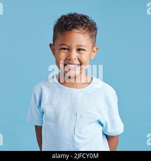 Porträt eines lächelnden kleinen braunen Jungen, der die Kamera anschaut. Glückliches Kind mit guten gesunden Zähnen für Zahn auf blauem Hintergrund Stockfoto