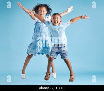 In voller Länge Porträt von niedlichen Mädchen und Jungen springen mit ihren Armen ausgestreckt und Spaß auf blauem Studio-Hintergrund. Glücklicher kleiner Bruder und Stockfoto