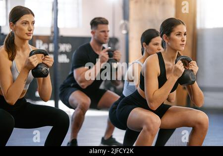Eine vielfältige Gruppe aktiver junger Menschen, die beim gemeinsamen Training in einem Fitnessstudio Kettlebell-Knieübungen machen. Fokussierte Athleten, die sich selbst herausfordern Stockfoto