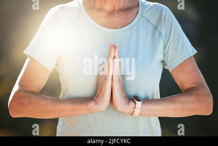 Nahaufnahme einer älteren Frau, die draußen mit verbundenen Händen in namastiger Position steht und in der Natur meditiert. Innere Ruhe, Balance und Leben finden Stockfoto