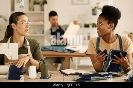 Zwei Modedesigner arbeiten zusammen. Diverse Geschäftsfrauen nähen zusammen in einem Studio. Schneiderinnen sprechen über Denim-Material. Zwei Stockfoto