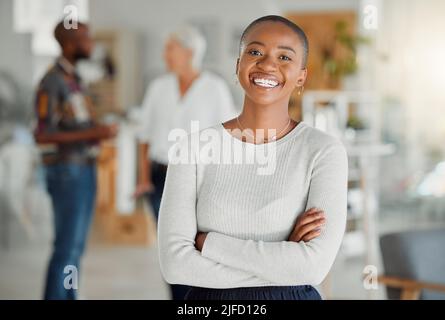 Porträt einer glücklichen afroamerikanischen Geschäftsfrau, die bei der Arbeit mit gekreuzten Armen steht. Eine selbstbewusste schwarze Managerin, die in einem Büro in steht Stockfoto