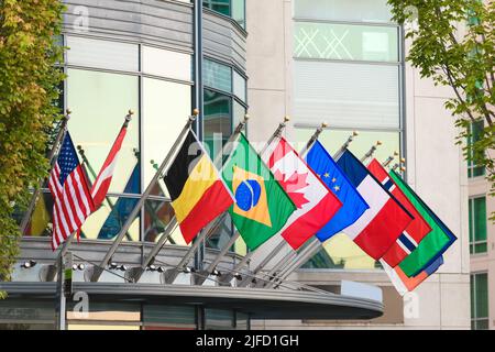 Reihe von Weltflaggen globaler Nationen, die an kurzen Fahnenmasten an einem Gebäude hängen Stockfoto